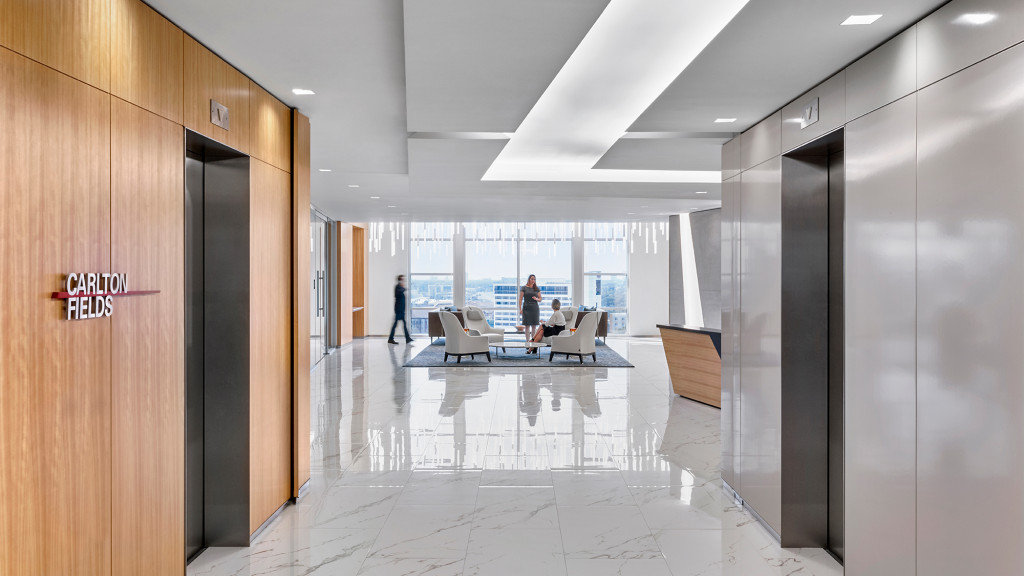 A room with a glass door and a couple of people sitting at a table with a laptop.